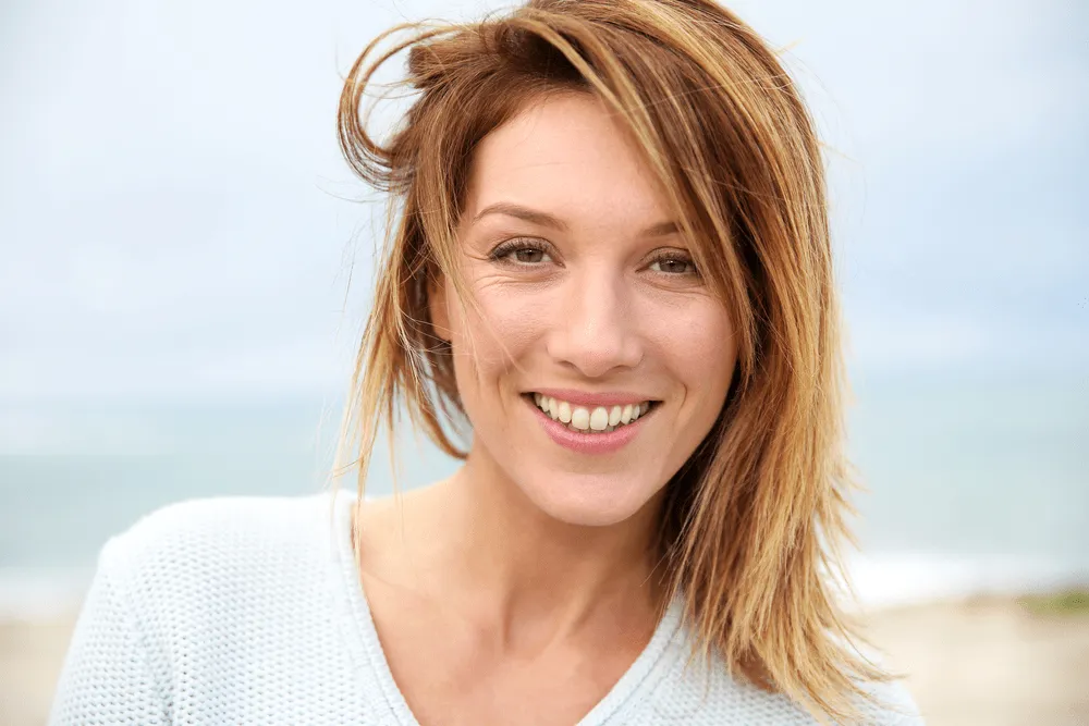 Smiling woman with natural makeup on a breezy beach day.