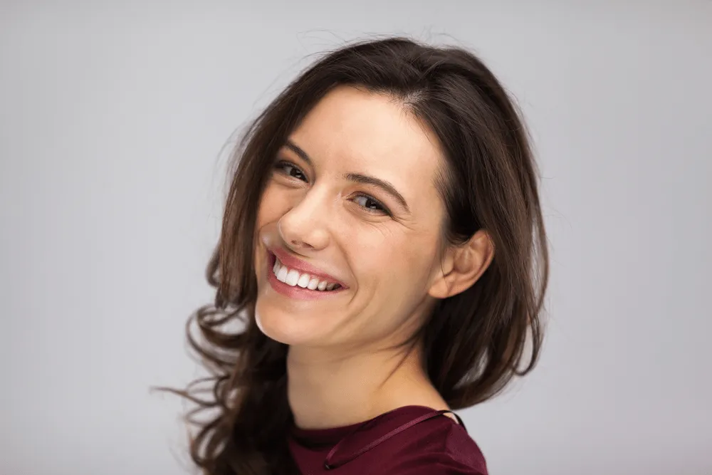 Woman with natural smile looking over shoulder on gray background.