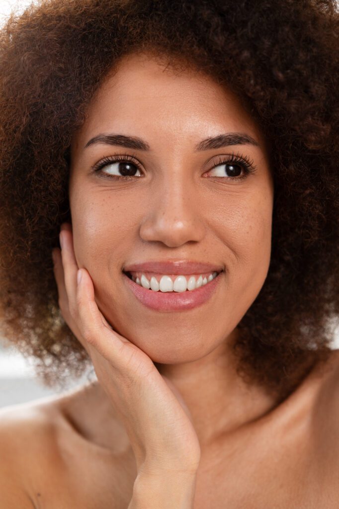 Close-up of woman with glowing skin and natural curls smiling.
