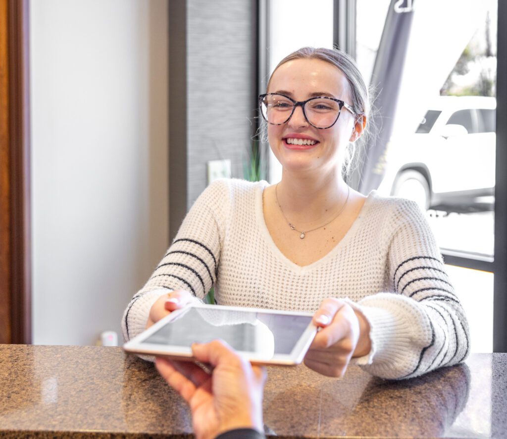 A friendly receptionist handing digital form to client at check-in.