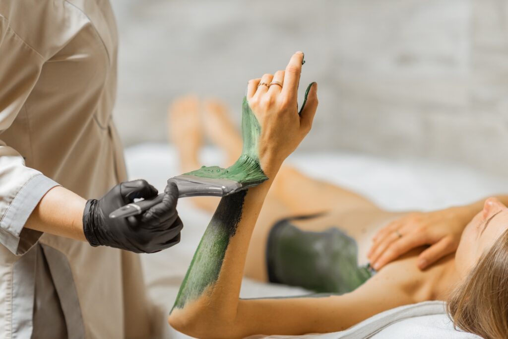 Spa therapist applying green body wrap to woman's arm.