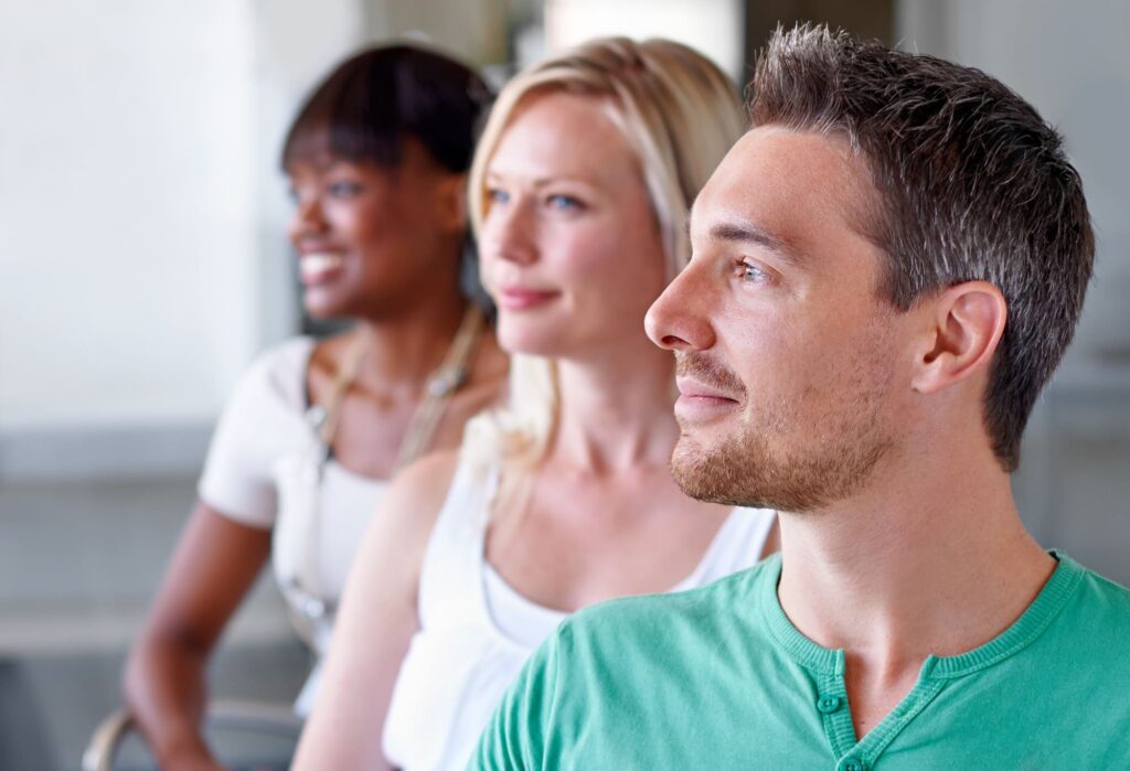 Three people sitting in a row, looking to the right, with the frontmost man in focus.